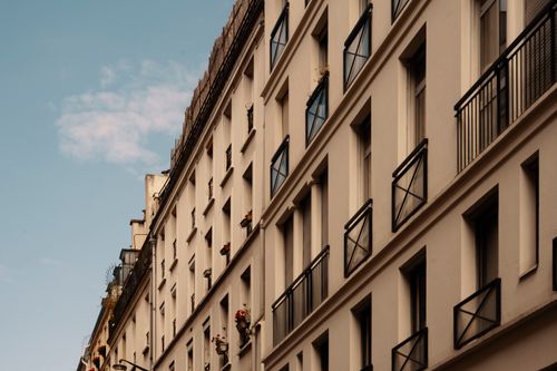 Free A beautiful street perspective of elegant, multi-story urban building with iron balconies against a blue sky. Stock Photo
