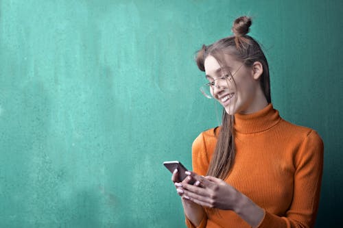 Woman in Orange Turtleneck Sweater Holding Black Smartphone