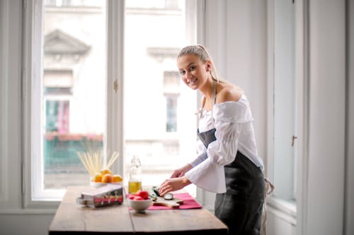 Woman in White and Black Off Shoulder Dress Standing Bedide Wooden Table