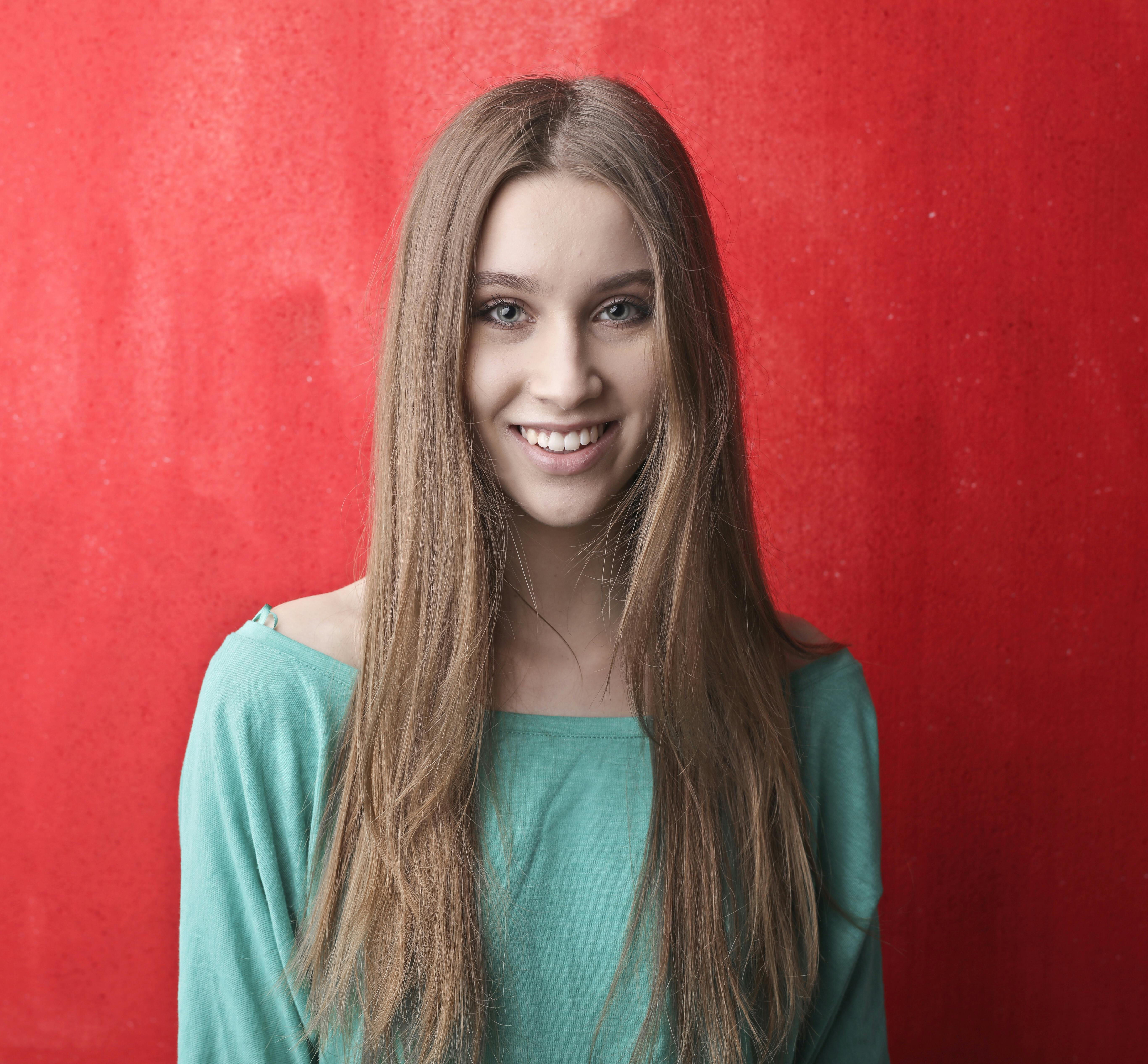 一位年轻女子留着长发，穿着绿色上衣，在鲜艳的红色背景下微笑着