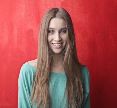 一位年轻女子留着长发，穿着绿色上衣，在鲜艳的红色背景下微笑着