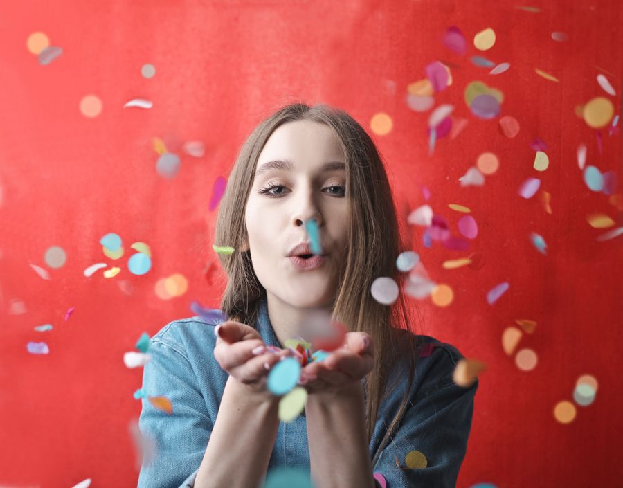 Woman joyfully blowing colourful confetti against a red backdrop