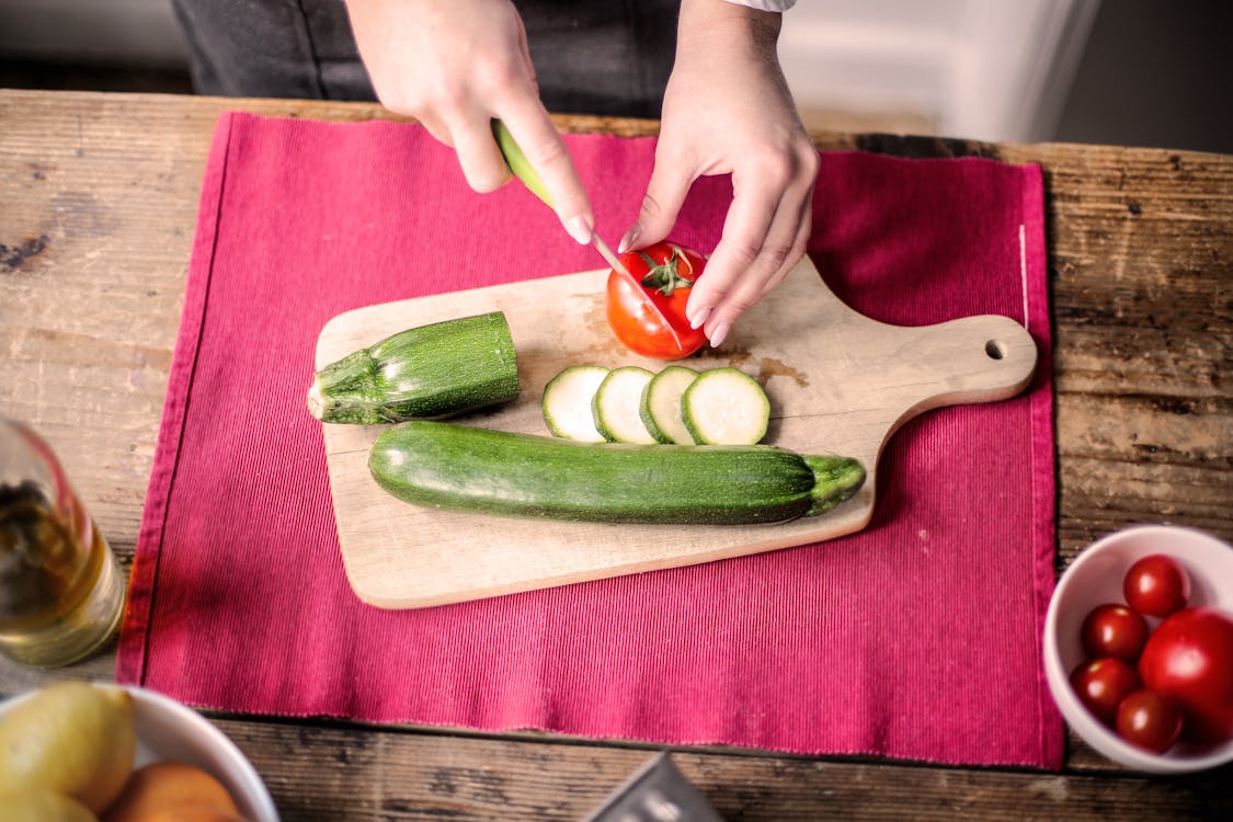 Person Slicing Tomato on Chopping Board