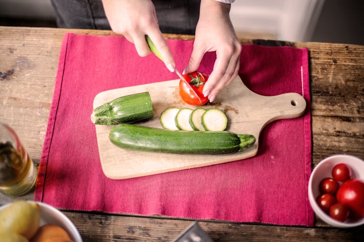 Person Slicing Tomato On Chopping Board