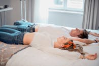 阳光明媚的卧室里，一对穿着休闲装的幸福情侣躺在床上，享受着无忧无虑的时光