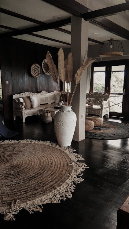 A room interior with a large white vase, dark wooden floors, and a rug.