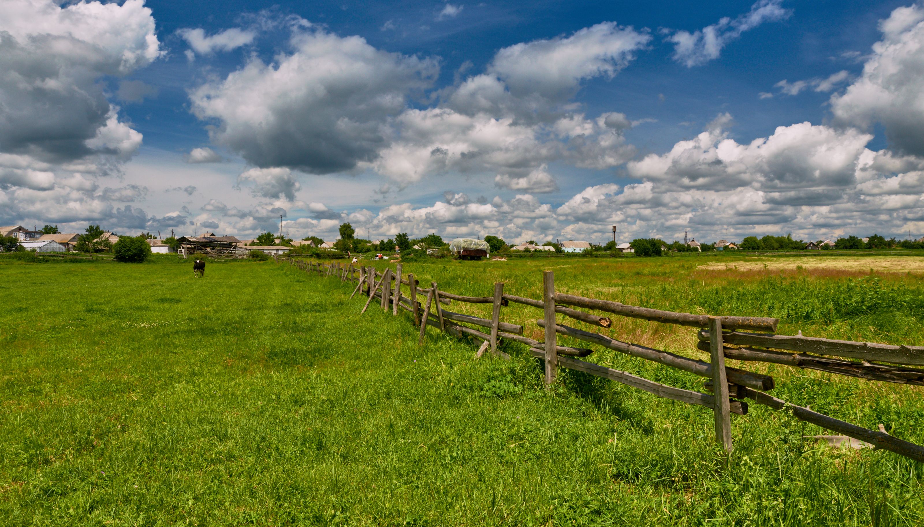 A picturesque rural scene with a wooden fence and lush greenery under a vibrant sky.