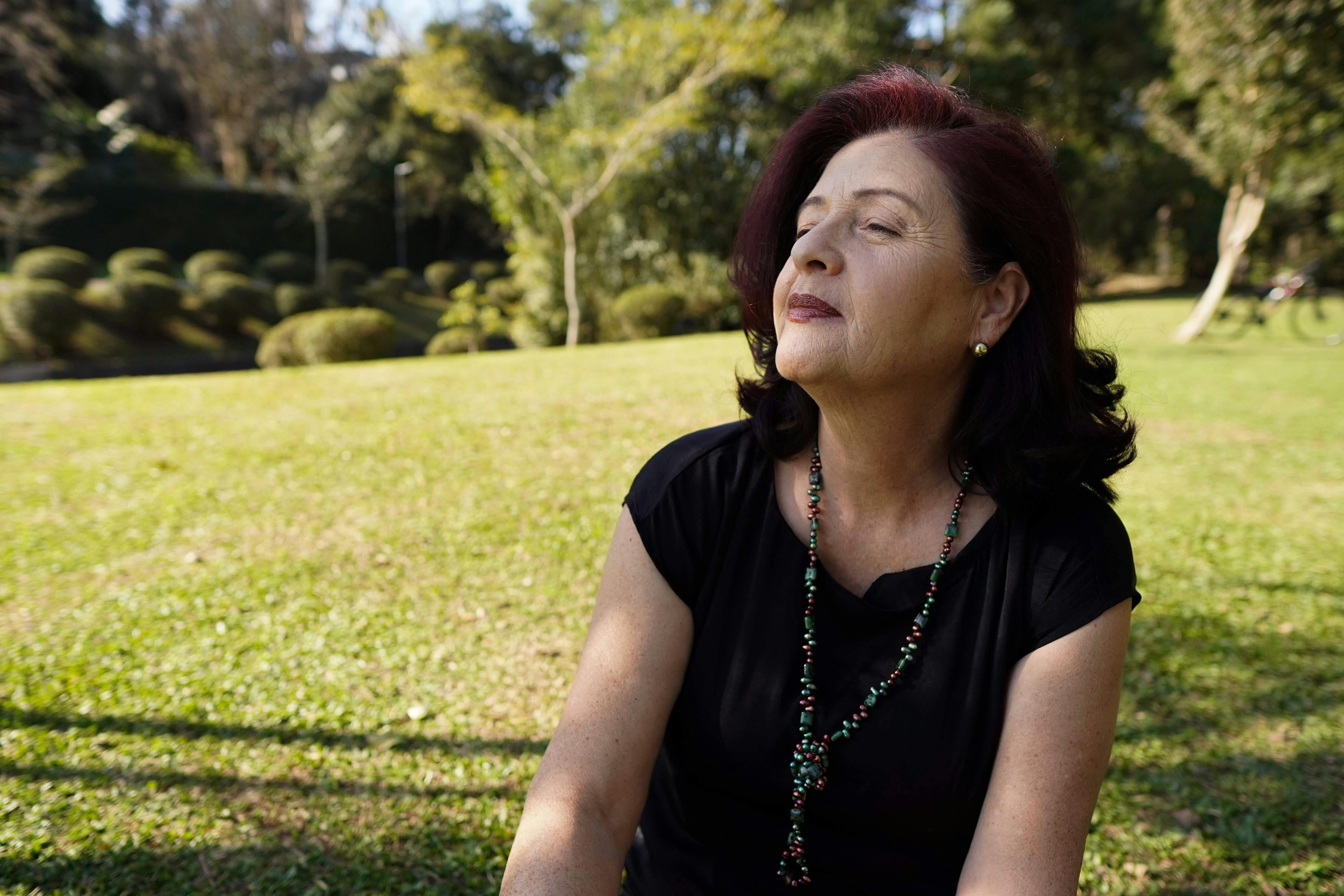 A relaxed, mature woman enjoys the sunlight in a tranquil park setting, exuding peace and contentment.