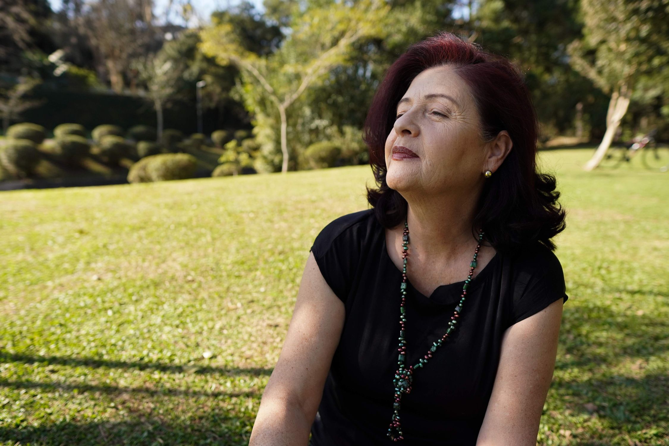 Mulher madura e relaxada desfrutando da luz do sol, simbolizando a sensação de bem-estar e serenidade mediada pela serotonina.
