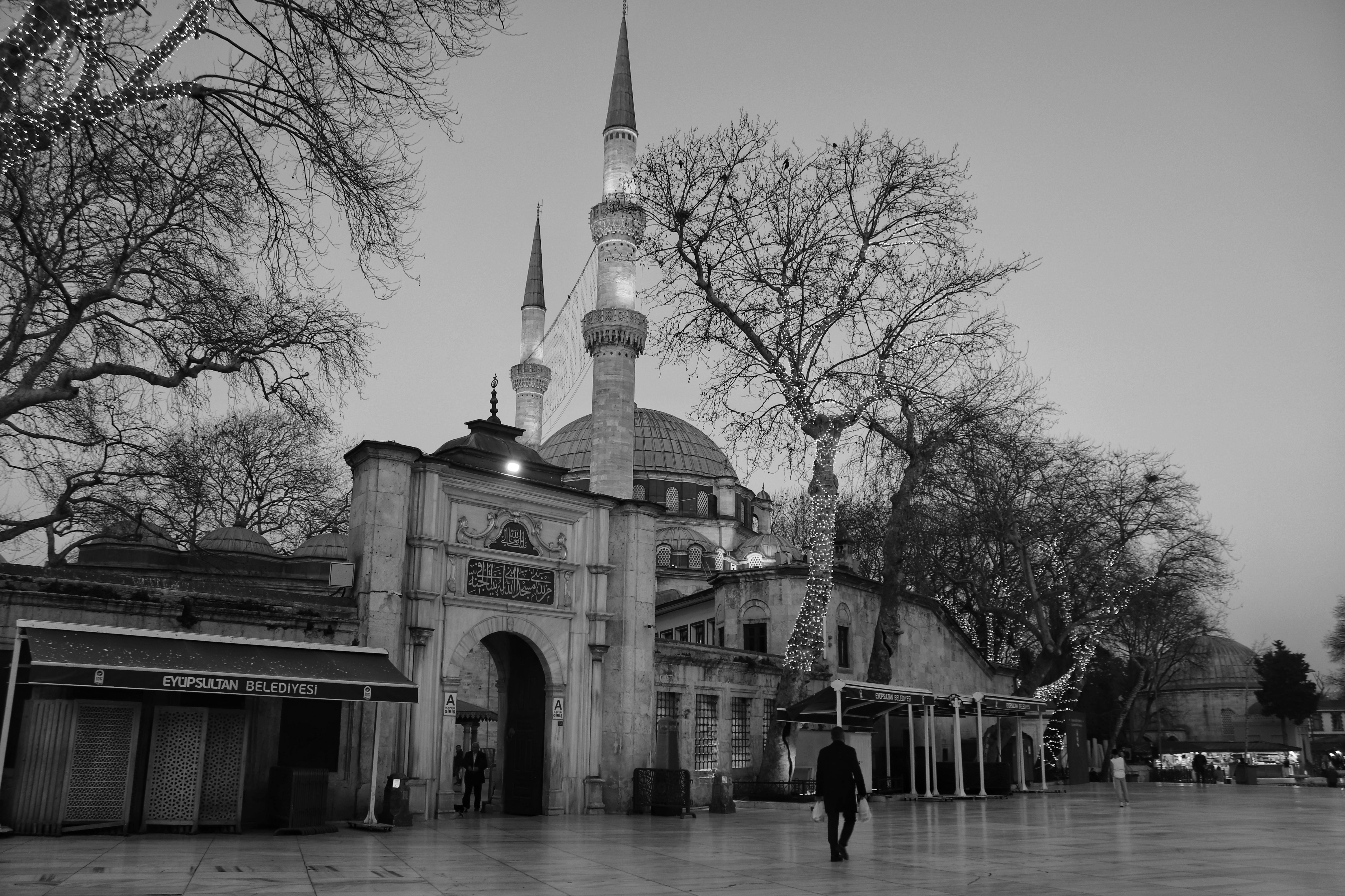 Serene black and white capture of Eyüp Sultan Mosque during evening with lights and empty plaza.