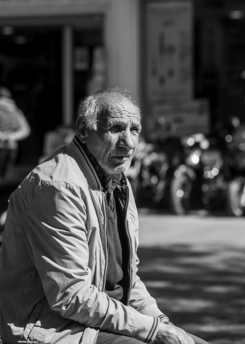 Free A contemplative senior man sitting in an outdoor urban setting under dappled sunlight. Stock Photo