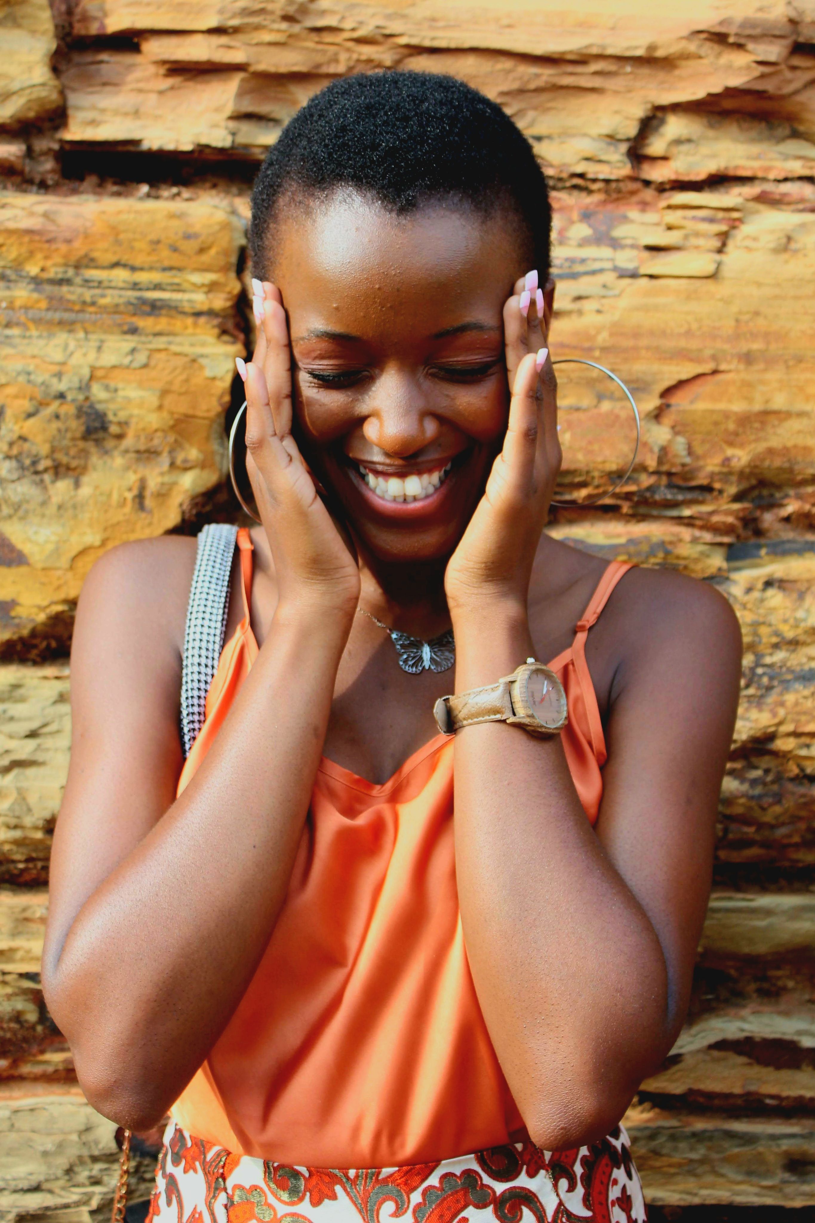 A woman joyfully smiles while standing against a textured wooden backdrop, expressing happiness.