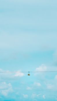 A solitary cable car travels across a pastel blue sky, creating a serene and minimalistic scene.