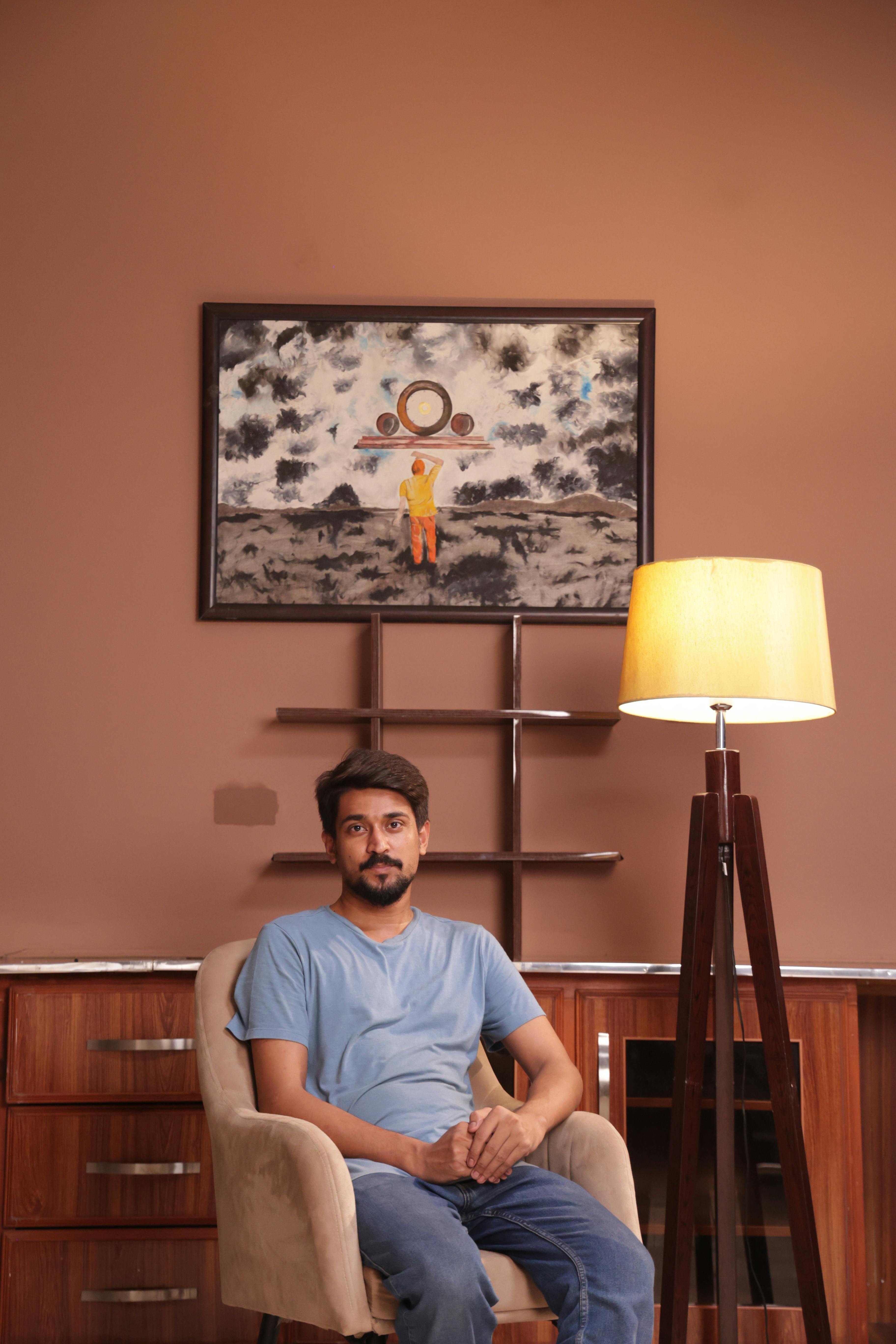 Casual man seated in modern room with art and lamp.