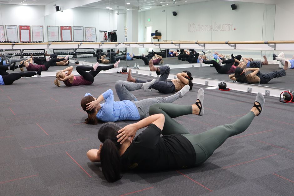 Group of adults participating in a vigorous indoor fitness class focused on core strength exercises.
