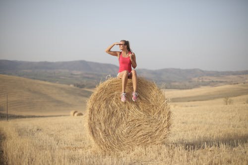 Woman in Pink Tank Top Sitting on Hay Roll