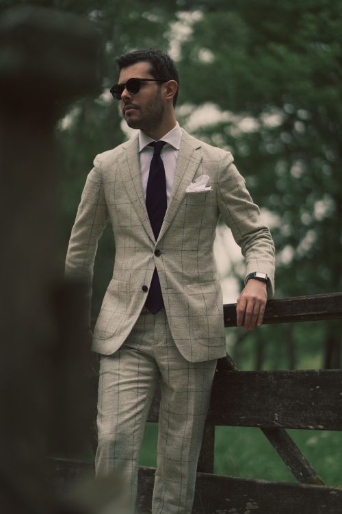 Free Portrait of a man in a checked suit leaning on a fence outdoors. Perfect for fashion and lifestyle imagery. Stock Photo