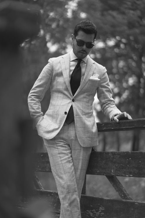 Free Man in elegant checkered suit leans on rustic fence, exuding sophistication. Stock Photo