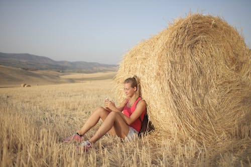 Woman in Pink Tank Top Leaning on Brown Hay Roll