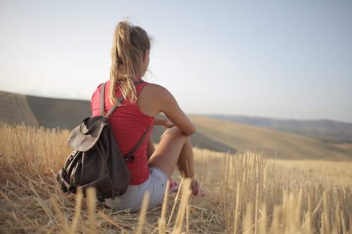 Woman With Leather Backpack While Sitting on Brown Grass Field