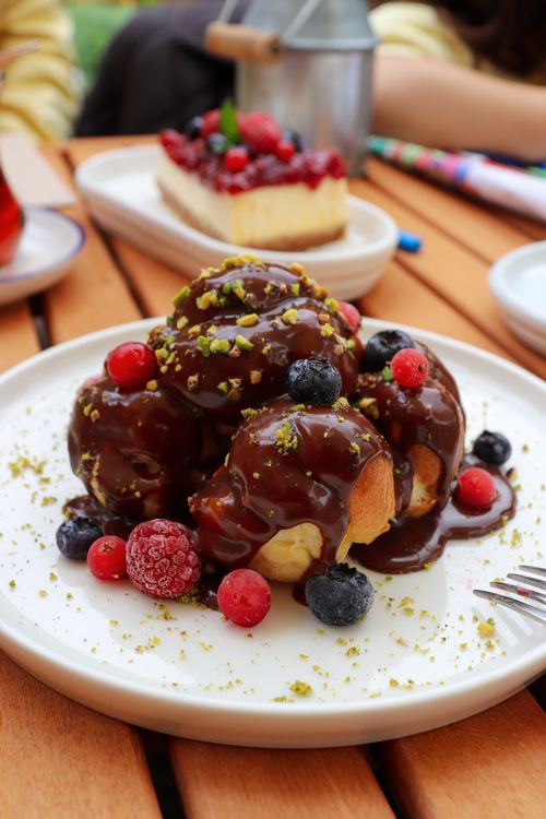 Free Tempting plate of profiteroles with chocolate sauce and fresh berries on a wooden table. Stock Photo