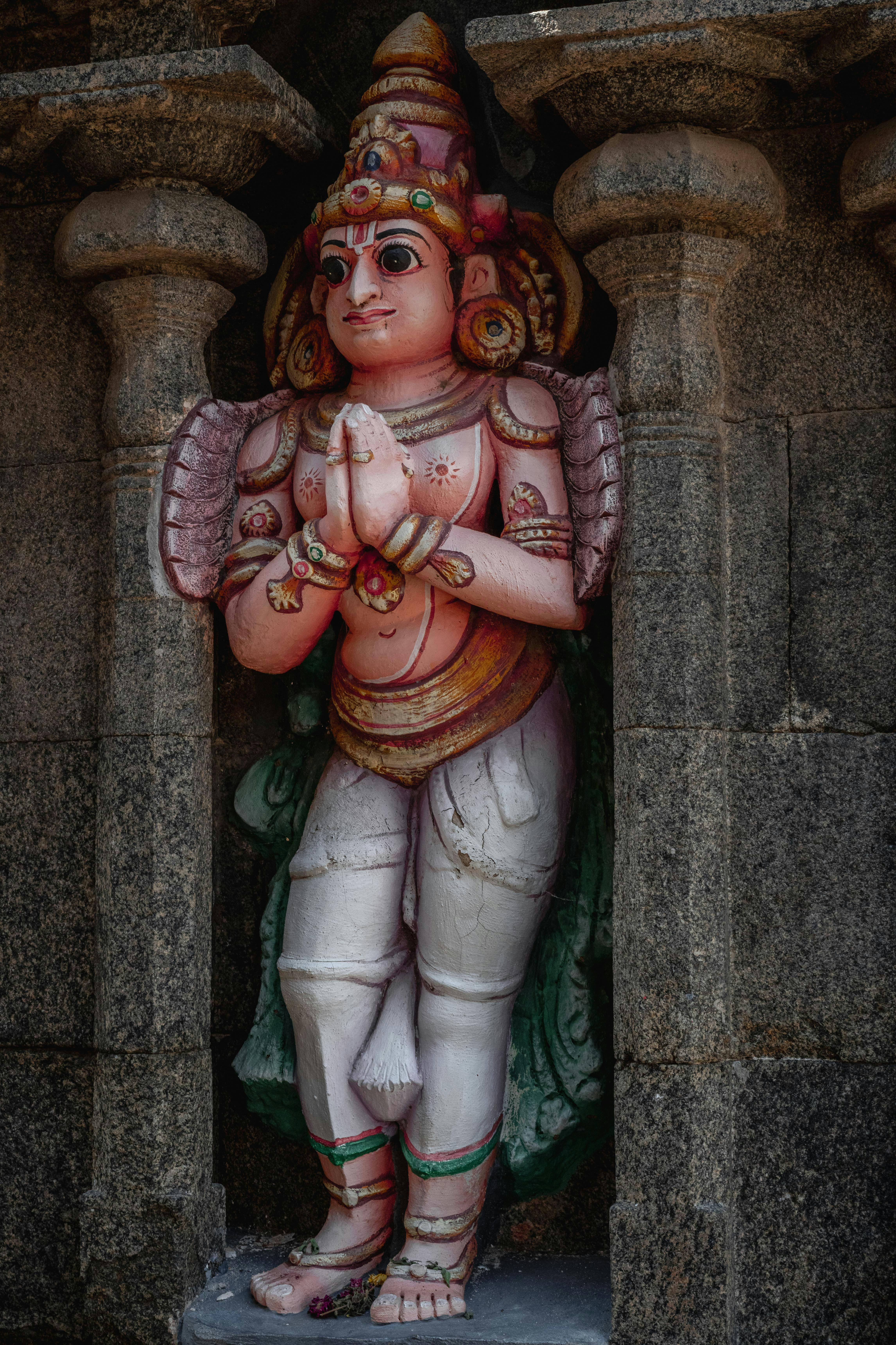 Detailed view of a colorful Hindu deity statue embedded within ancient stone temple architecture.