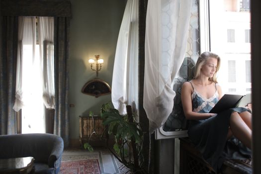 Woman in a blue dress reading by a window, enjoying leisure time indoors.. woman, blue, dress
