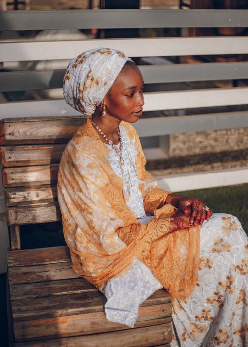 Free A serene portrait of a Nigerian woman in traditional attire sitting on a wooden bench outdoors. Stock Photo