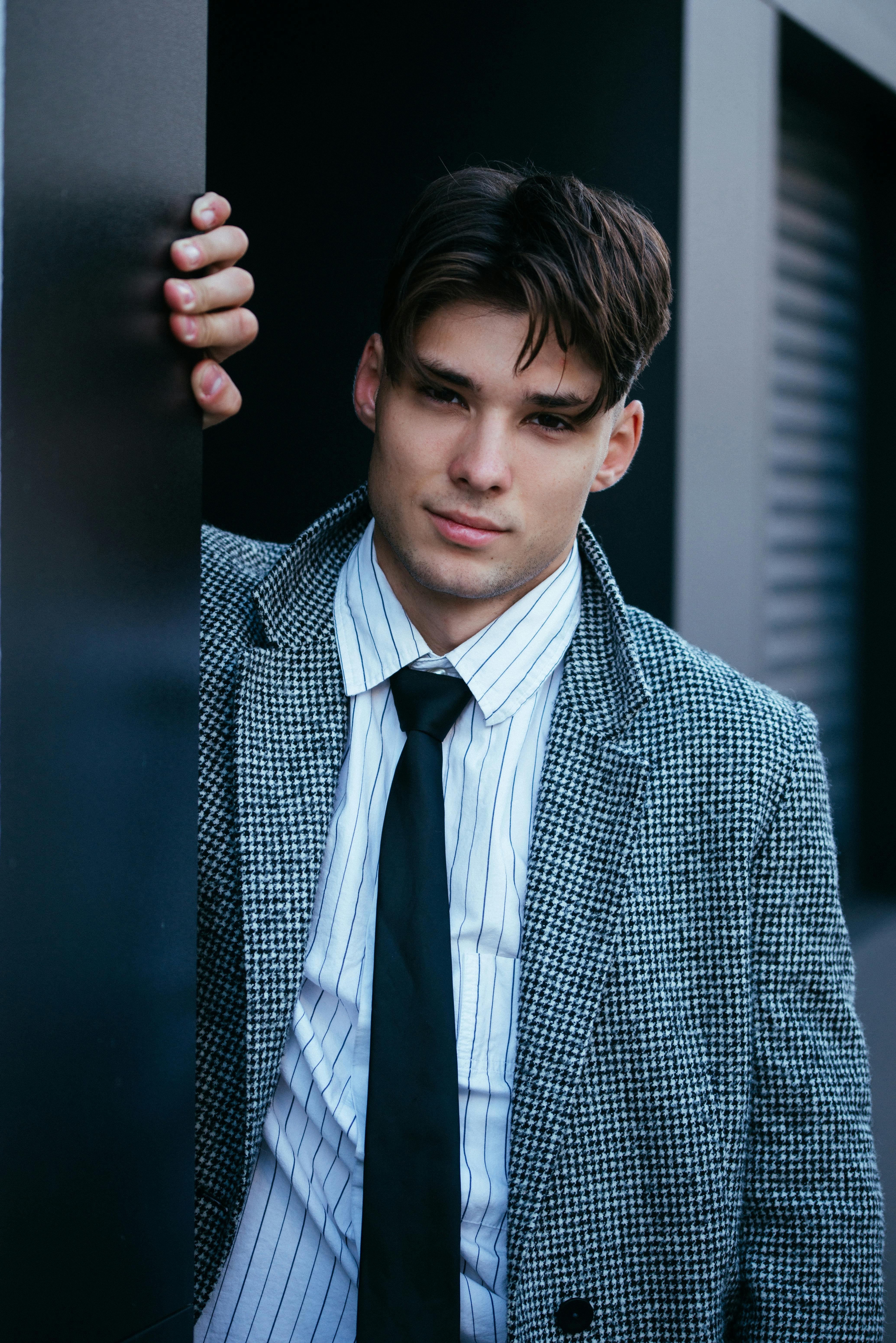 Confident young man wearing a blazer, striped shirt, and tie in an urban setting.