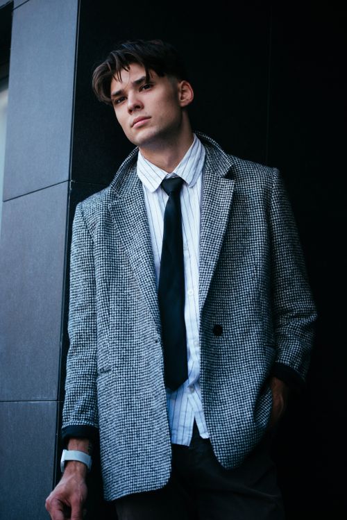 Free Fashionable young man in a blazer and tie, posing confidently with a dark urban background. Stock Photo