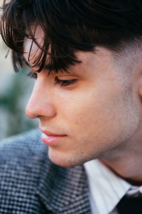 Free Close-up portrait of a young man in a blazer looking down thoughtfully outdoors. Stock Photo