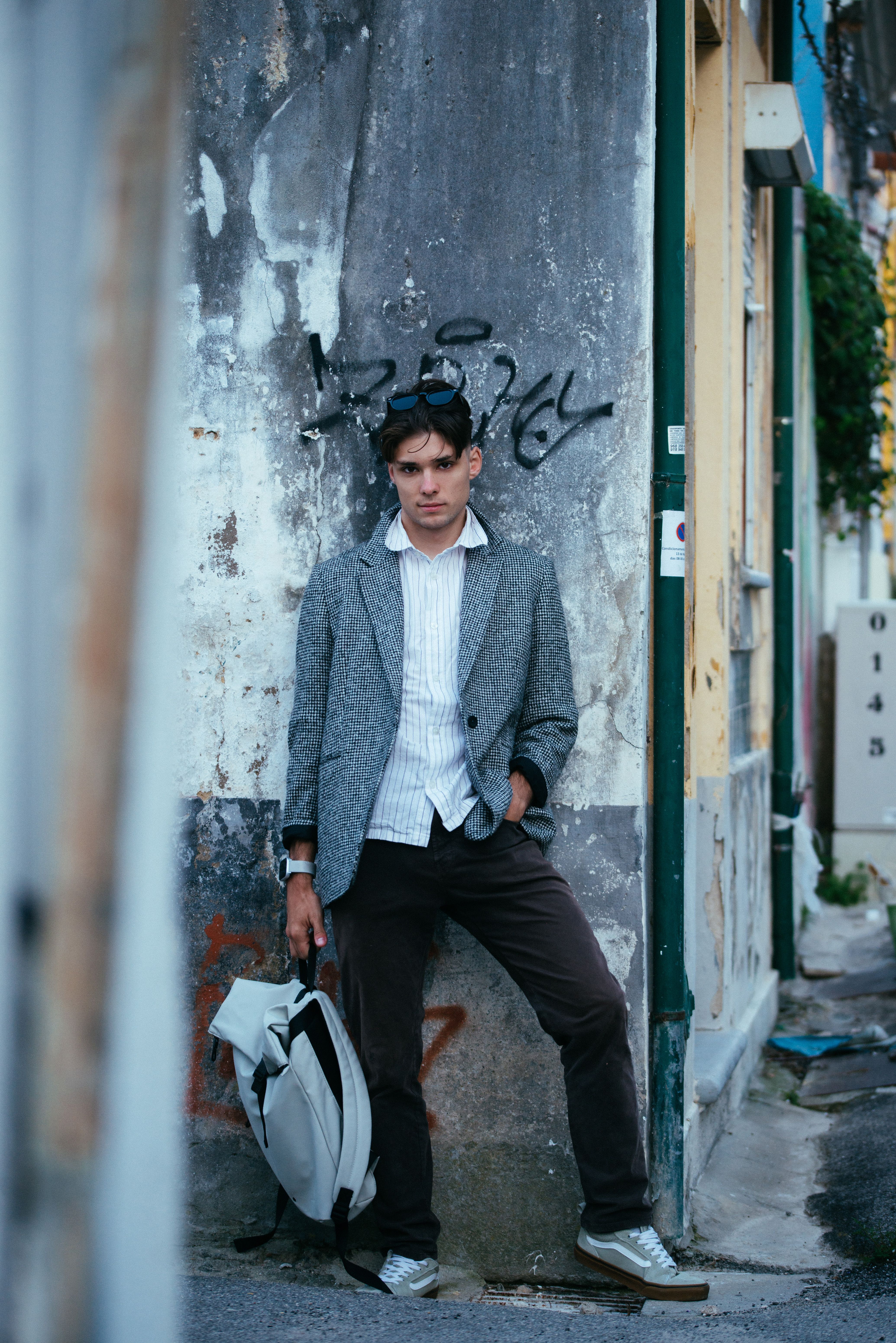 A stylish young man wearing a blazer and striped shirt poses in an urban street setting with a cool and confident look.