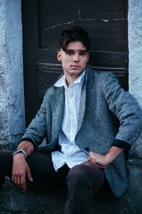 Free Confident young man wearing a blazer and striped shirt, posing outdoors against a textured backdrop. Stock Photo