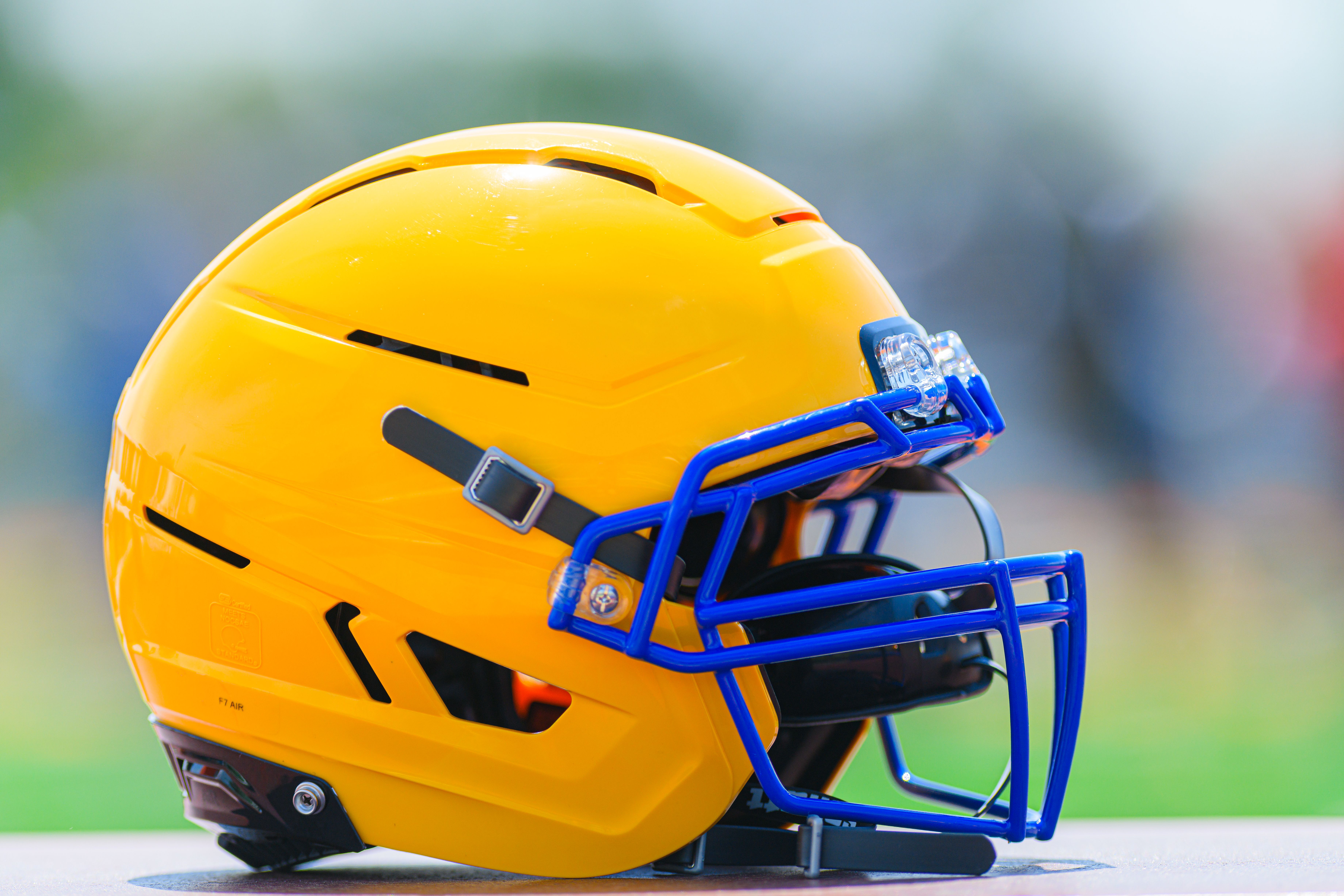 NCAA Football photo featuring Close-up of a bright yellow football helmet on an outdoor field under daylight.