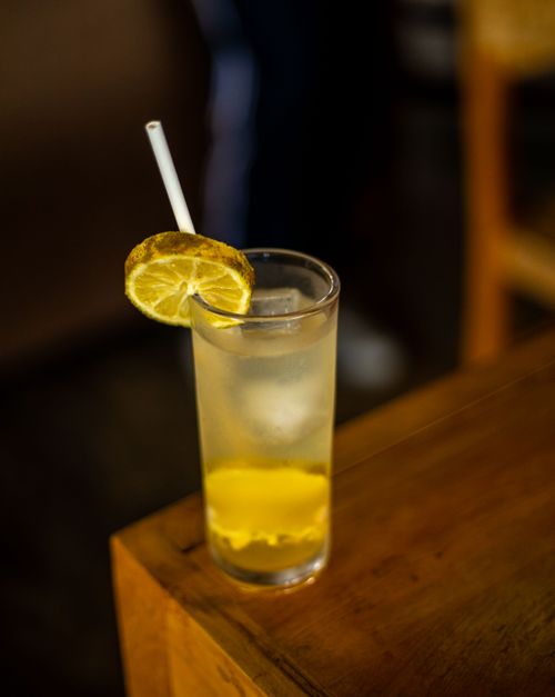 Free Tall glass of iced lemon drink with straw, garnish, and wooden table setup. Stock Photo