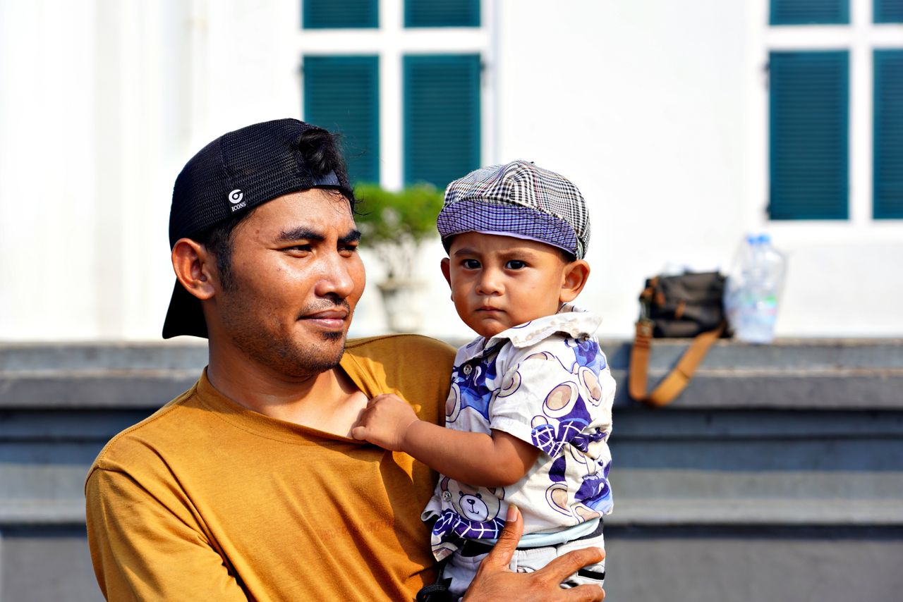 a father holds his young son while enjoying a sunny day outdoors