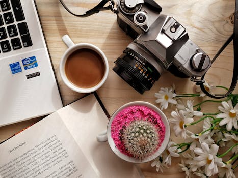 这是一个配有咖啡、老式相机、书籍、笔记本电脑和仙人掌的平面创意工作区