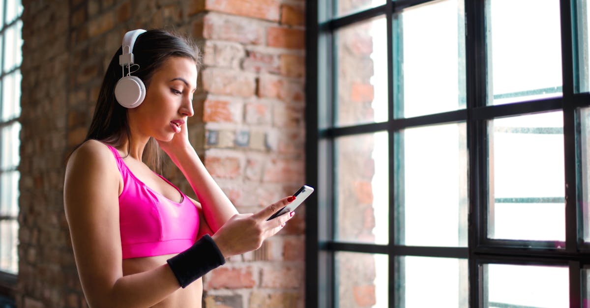 Woman in sports wear listening to music on headphones while holding a smartphone indoors.
