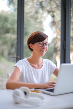 一位短发女性在室内愉快地使用笔记本电脑，展现了远程工作的生活方式