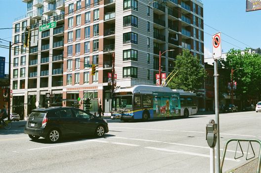 Street scene in Vancouver featuring a modern bus, cars, and urban architecture under a clear blue sky.