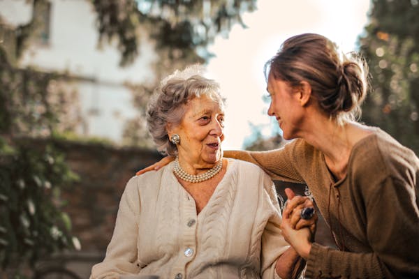 Caregiver assisting elderly woman in wheelchair outdoors