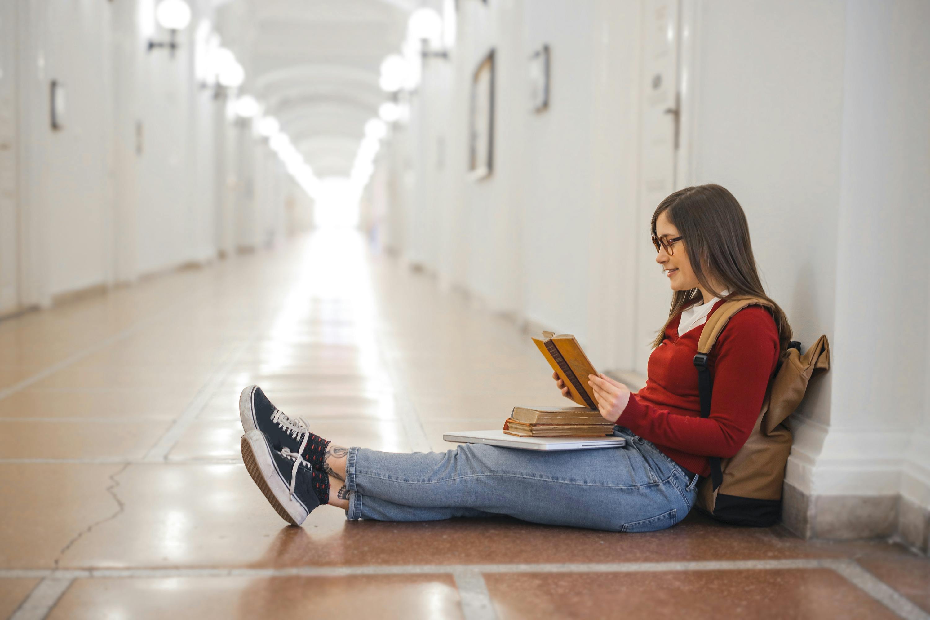 photo of woman sitting on hallway while reading a book