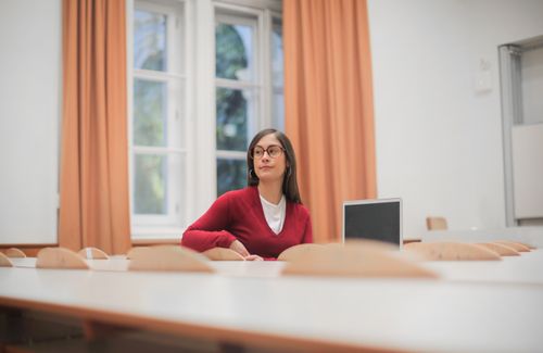 Free Woman in red sweater sitting at desk in modern office, looking away thoughtfully. Stock Photo