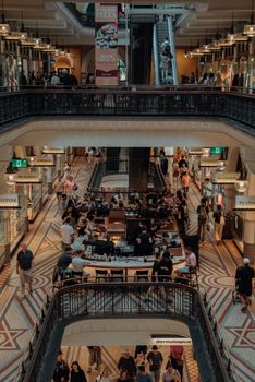 View of a busy shopping arcade in Sydney with shops, escalators, and people enjoying their day.
