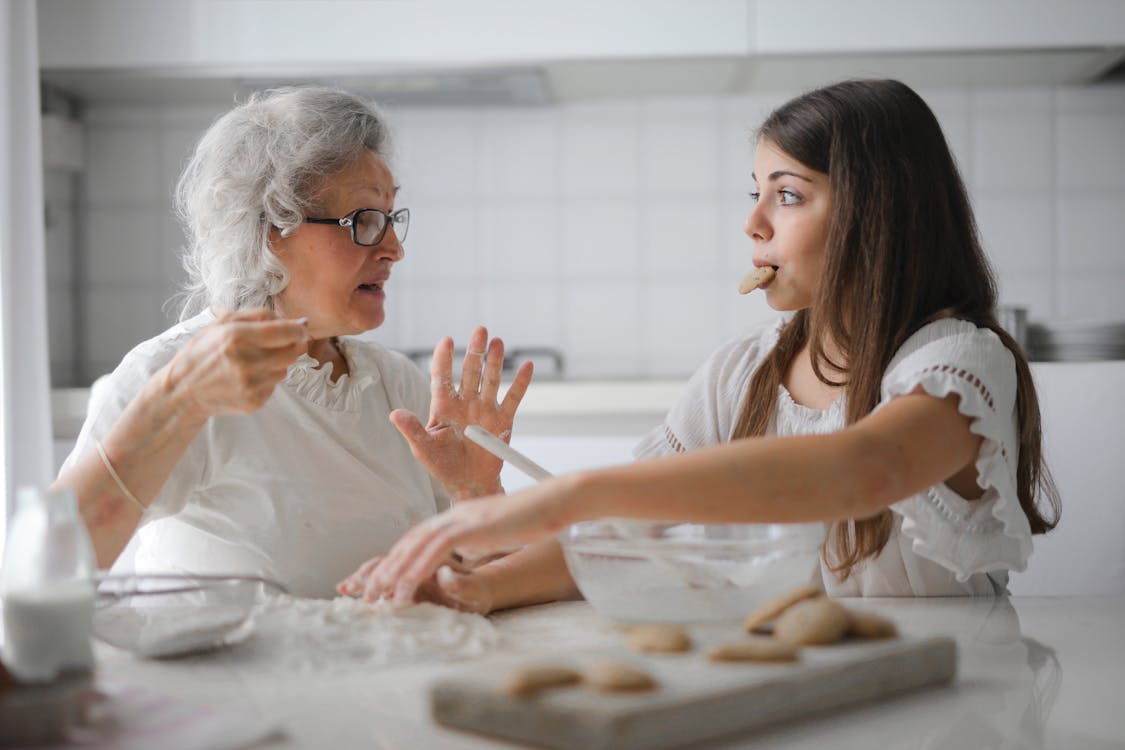 明るいモダンなキッチンで一緒に料理をしながら面白い会話をしている孫娘と物思いにふける祖母