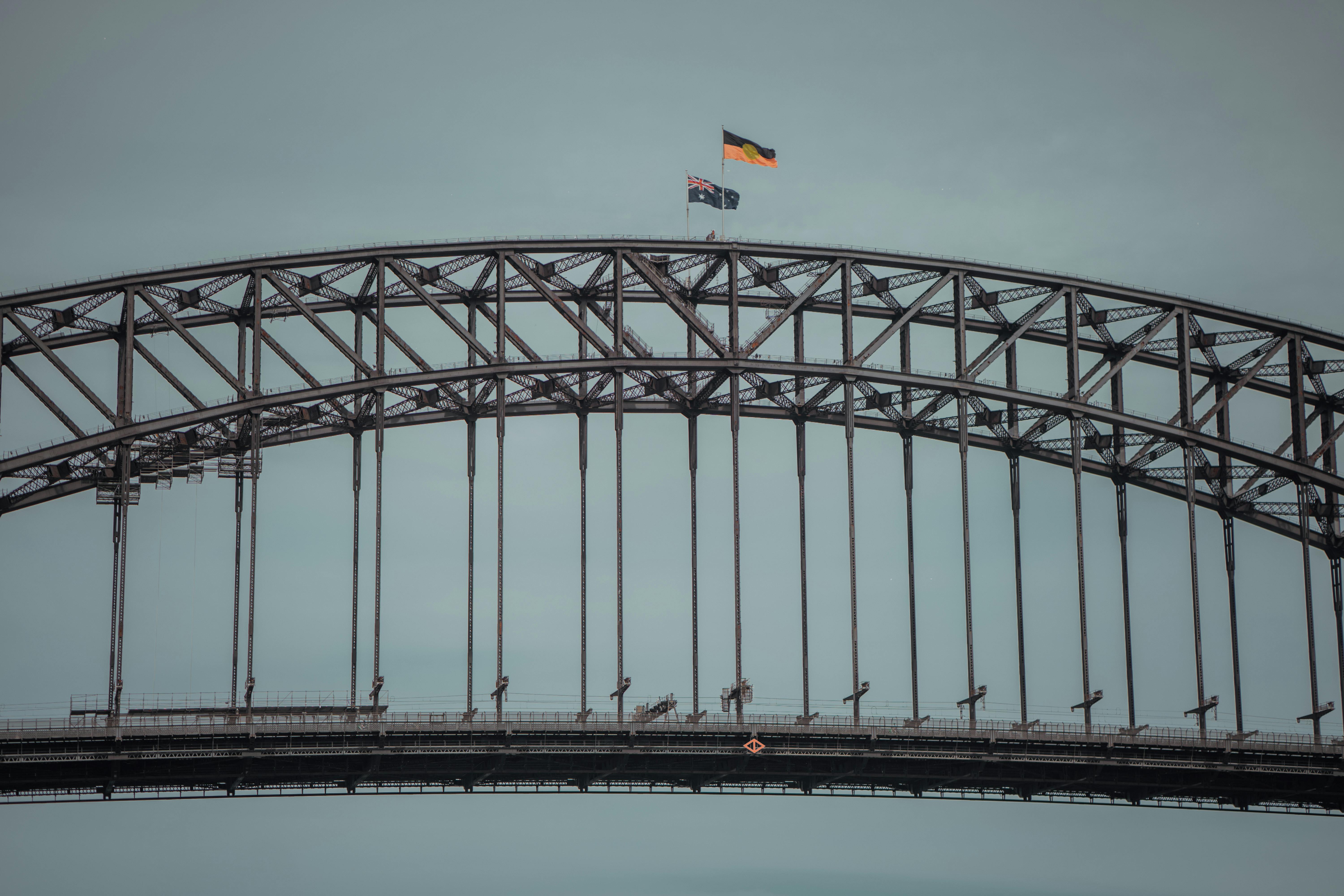 Sydney Harbour Bridge close-up + Australian flags — 1932 134m steel arch + BridgeClimb summit + pedestrian free