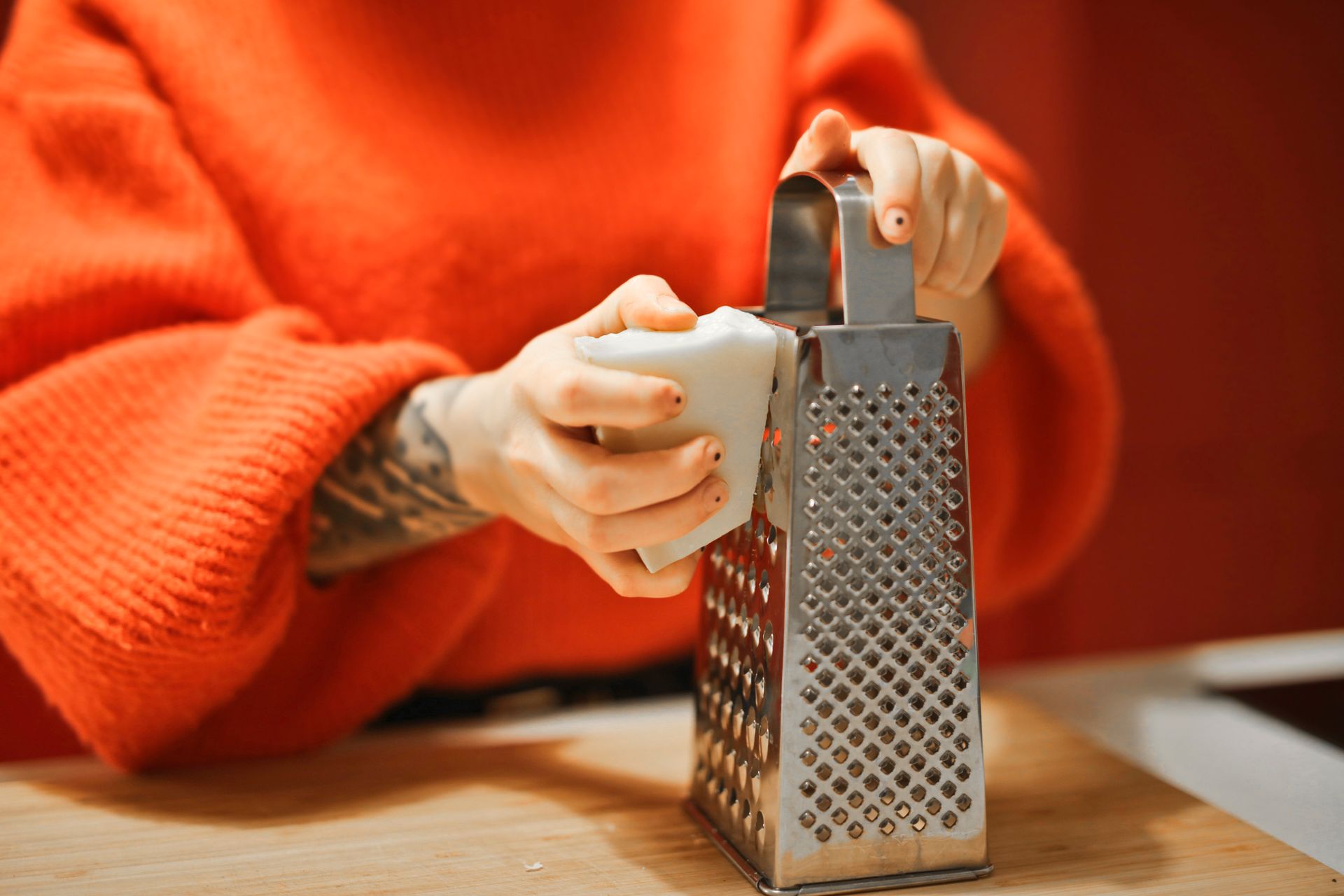Person grating bar of soap with metal grater in kitchen, showcasing a hygiene concept.