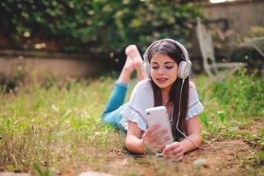 Young woman lying on grass with headphones and smartphone, enjoying a leisure moment outdoors.