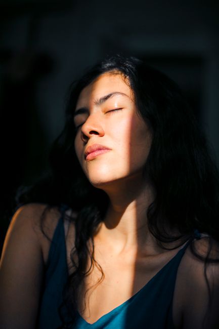 Close-up portrait of a woman with eyes closed, bathed in soft sunlight and shadows.