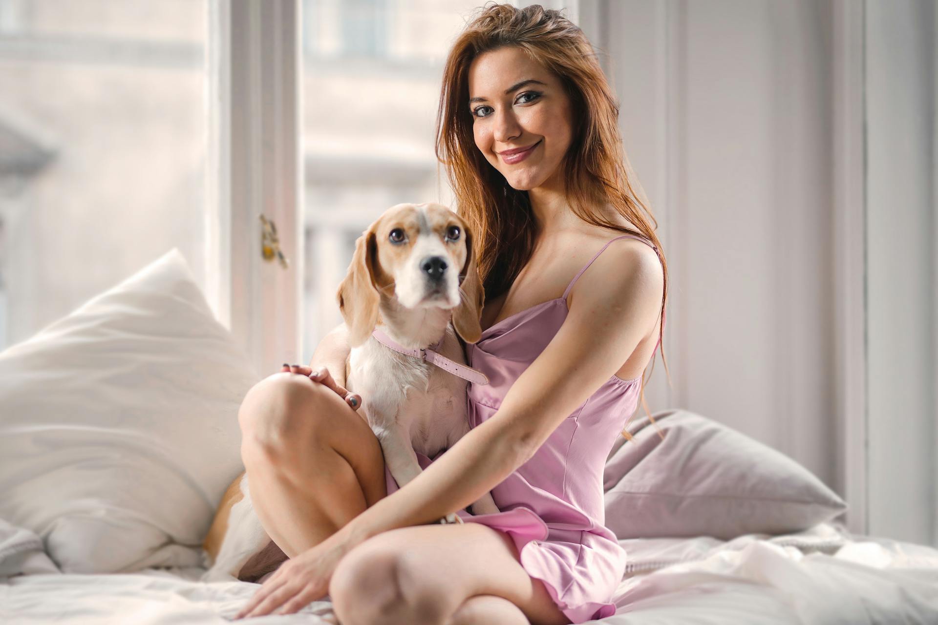 Woman in Pink Dress Sitting on Bed With White and Brown Short Coated Dog